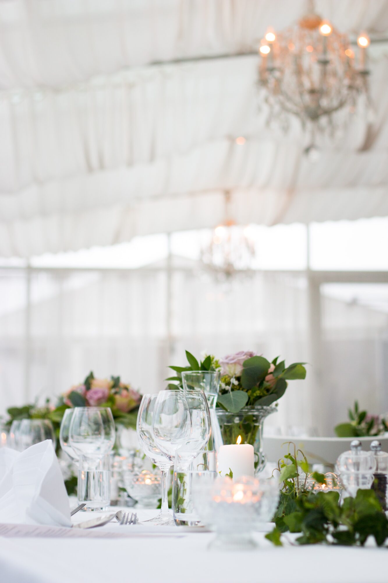 Table élégamment dressée avec des verres à vin et des fleurs, dans une salle lumineuse décorée de chandeliers.