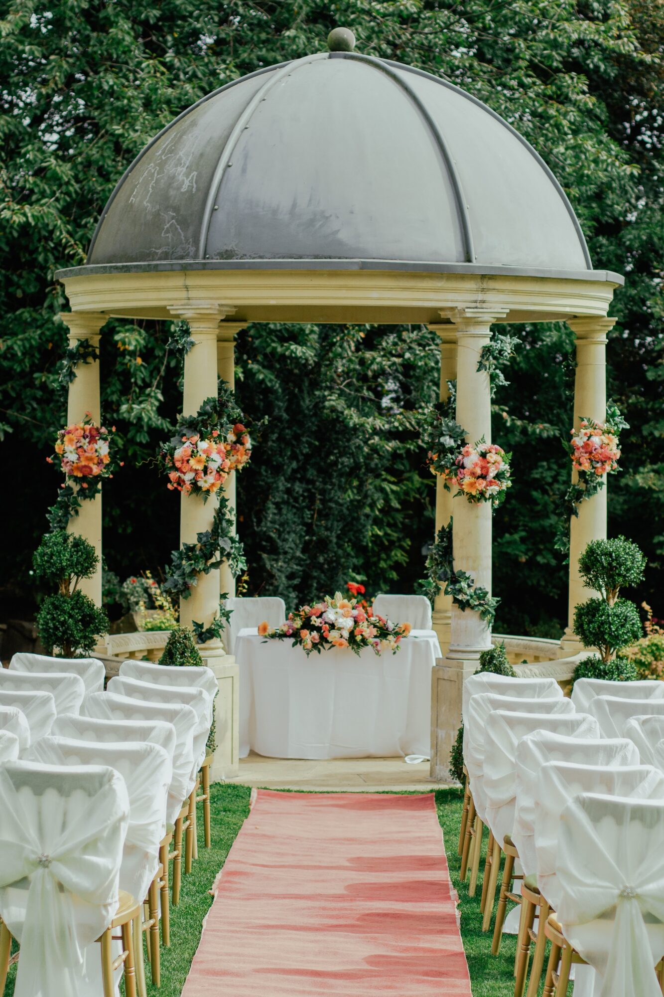 Allée de mariage avec chaises blanches menant à un autel décoré sous une pergola.